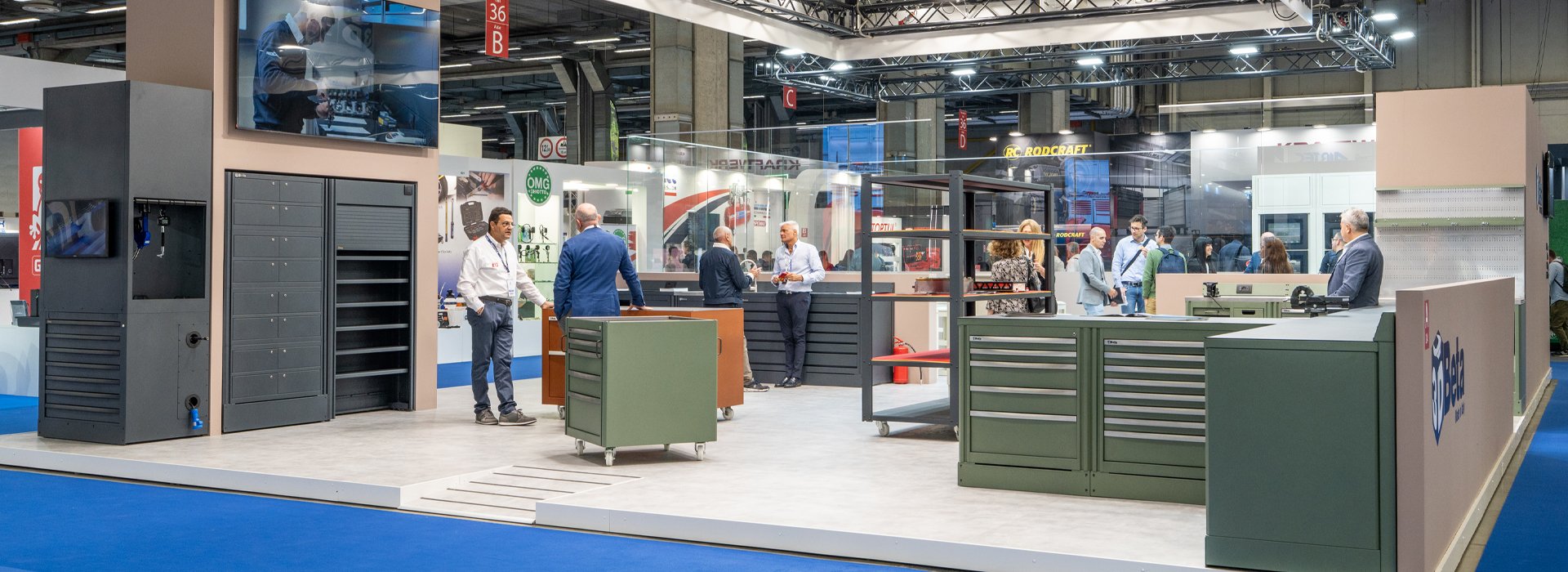 Mobili da officina di 3D Beta esposti mentre le persone interagiscono allo stand di Autopromotec 2025