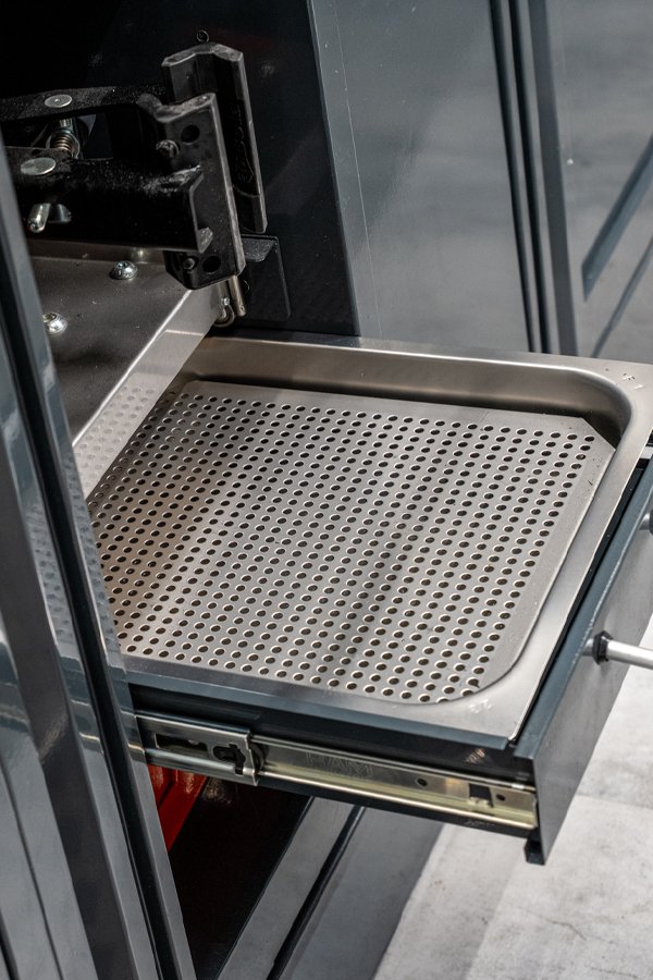 L'arredamento dell'officina comprende un vassoio metallico perforato che fuoriesce da un'unità forno dell'officina 3D Beta.
